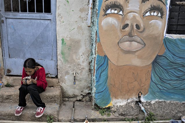 A girl sits with a cat next to a mural, in the San Agustin neighborhood, in Caracas, on April 8, 2023. Dozens of artists beautify the San Agustin neighborhood with murals, graffiti and paintings as a project to recover and revitalize physical and symbolic spaces in the neighborhood. It is an urban proposal exercised from the cultural organization of the neighborhood “where street artists assume militancy for beauty as a strategy of popular work based on valuing the physical spaces that build social and cultural identity” and in this way keep crime away by attracting tourists from all over the world to this popular area in West Caracas. (Photo by Pedro Rances Mattey/Anadolu Agency via AFP Photo)