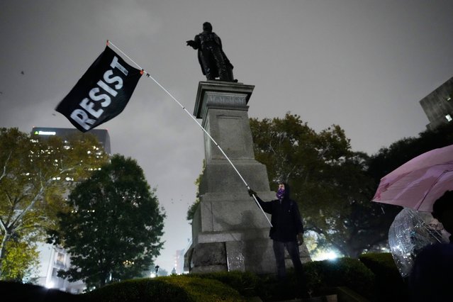 A protestor waves a flag in a pouring rain during a demonstration against an impending Customs and Border Patrol immigration crackdown in New Orleans, Monday, December 1, 2025. (Photo by Gerald Herbert/AP Photo)