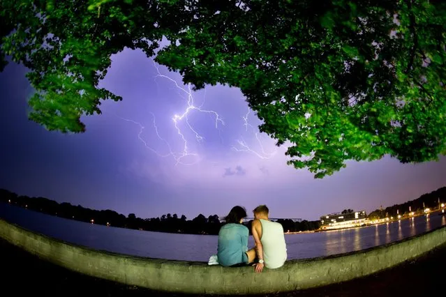 A young couple sit on the banks of the Maschsee lake as lightnings are seen in the sky over Hanover, central Germany, on June 20, 2013. (Photo by Julian Stratenschulte/AFP Photo)