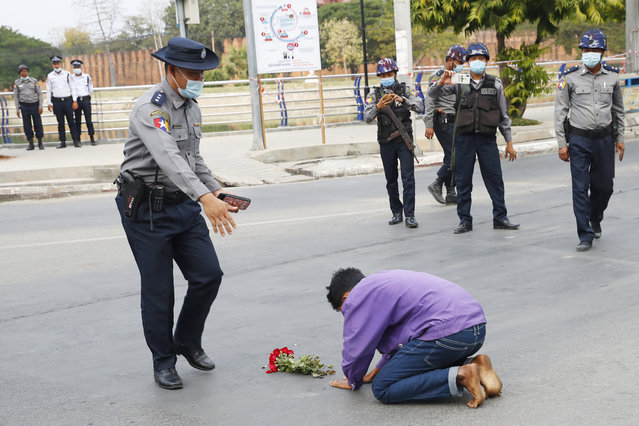 A protest supporter offers flowers and kneels on a road before a police officer in Mandalay, Myanmar, on February 6, 2021. Protests in Myanmar against the military coup that removed Aung San Suu Kyi’s government from power have grown in recent days despite official efforts to make organizing them difficult or even illegal. (Photo by AP Photo/Stringer)