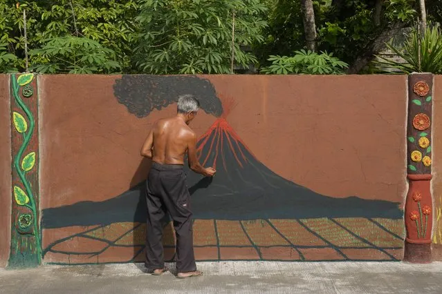 Violeta Peralta paints a picture of an erupting Mayon Volcano outside his home in Legaspi, Albay province, northeastern Philippines, Sunday, June 11, 2023. Thousands of villagers have been forced to leave rural communities within a 6-kilometer radius of Mayon volcano's crater in Albay province which was placed under a state of calamity on Friday to allow more rapid disbursement of emergency funds in case a major eruption unfolds. (Photo by Aaron Favila/AP Photo)