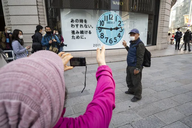 A woman takes a photo of her husband in front of a clock that shows 2:46 p.m. to commemorate the 2011 earthquake that hit the northeastern Japan, before the 10th anniversary to pay tribute to the victims in Tokyo Thursday, March 11, 2021. (Photo by Hiro Komae/AP Photo)
