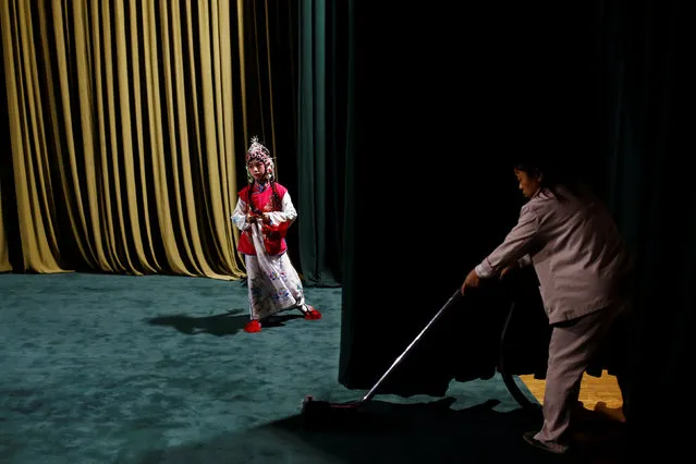 A cleaner vacuums the stage as a participant prepares to perform during a traditional Chinese opera competition at the National Academy of Chinese Theatre Arts in Beijing, China, November 26, 2016. (Photo by Thomas Peter/Reuters)