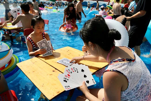 People sitting inside a swimming pool play giant cards at a water park on a hot day in Chongqing, China on August 19, 2018. (Photo by Reuters/China Stringer Network)