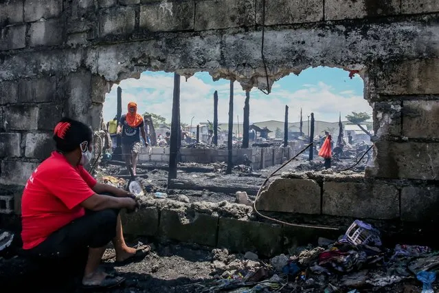 A woman looks through a large hole on a concrete wall as she rests from searching for her belongings from charred home after a fire at a slum area in Rizal Province, the Philippines on March 26, 2021. The Philippine Bureau of Fire Protection said that the fire is believed to have started from one of the houses that was being used as a garment manufacturing area, leaving more than 170 families homeless in the fire. (Photo by Rouelle Umali/Xinhua News Agency/Imago)