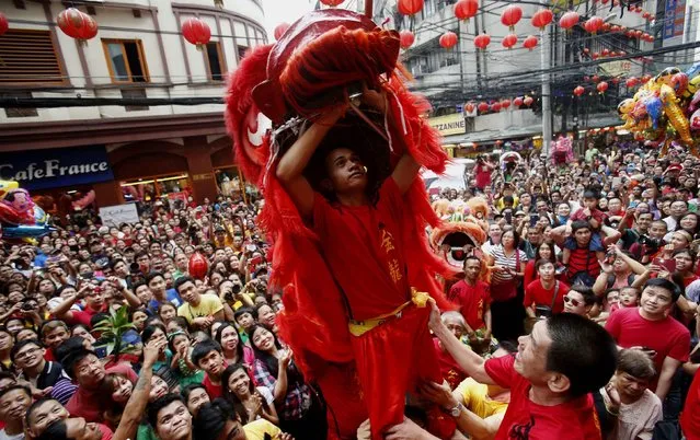 A lion dance performer waits for “Ang Pao”, or a money gift, in front of a grocery next to revellers as they celebrate Lunar New Year at Manila's Chinatown February 19, 2015. (Photo by Erik De Castro/Reuters)