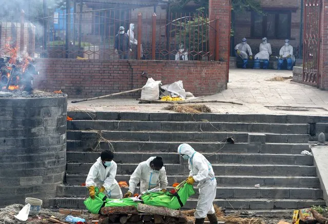 Nepalese workers wearing personal protective suits place the body of a COVID-19 victim on a funeral pyre for cremation on the banks of Bagmati river in Kathmandu, Nepal, Friday, May 7, 2021. Across the border from a devastating surge in India, doctors in Nepal warned Friday of a major crisis as daily coronavirus cases hit a record and hospitals were running out of beds and oxygen. (Photo by Niranjan Shrestha/AP Photo)