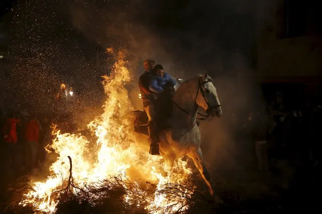 A man rides a horse with a child through the flames during the “Luminarias” annual religious celebration on the eve of Saint Anthony's day, Spain's patron saint of animals, in the village of San Bartolome de Pinares, northwest of Madrid, Spain, January 16, 2016. (Photo by Susana Vera/Reuters)