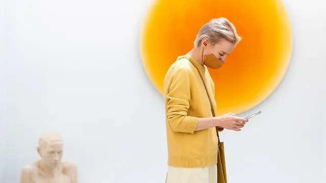 A visitor walks past a painting while looking at her phone during Art Madrid 21 Exhibition on May 26, 2021 in Madrid, Spain. (Photo by Samuel de Roman/Getty Images)