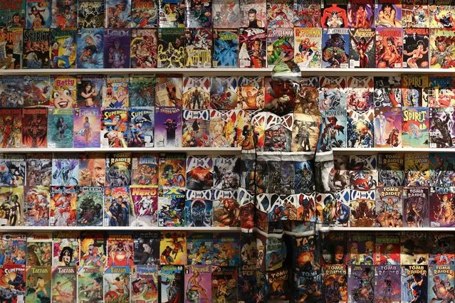 Liu Bolin, a Chinese artist, blends himself into the background in front of a shelf lined with comic books in Caracas, on November 3, 2013. (Photo by Jorge Silva/Reuters)