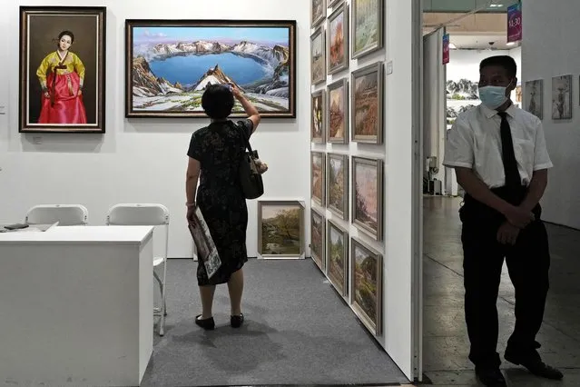 A security guard stands watch as a visitor takes a photo of a painting depicting snow-capped Mount Baekdu, the mythical birthplace of the Korean people, at the booth for The Paintings Say Arirang gallery that trumpets itself as China's premier seller of North Korean art, in Beijing, September 8, 2023. The gallery's existence and conspicuous sales tactics, experts say, highlight China's lax enforcement of U.N. sanctions targeting North Korea to stymie Pyongyang's nuclear program. (Photo by Ng Han Guan/AP Photo)