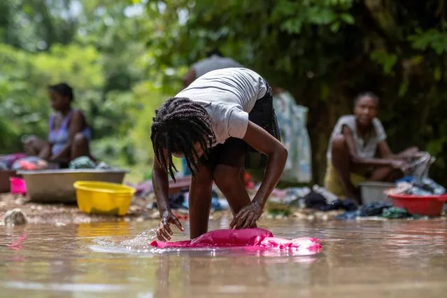 A girl washes clothes in a river in the Camp Perrin neighborhood in, Les Cayes, Haiti on August 22, 2021. (Photo by Ricardo Arduengo/Reuters)