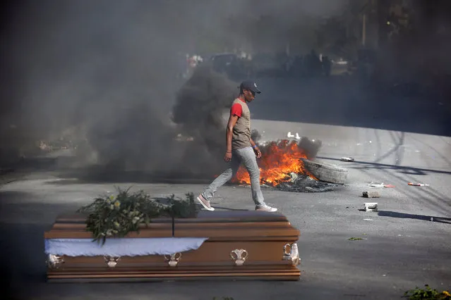 A man walks past burning tires and one of the caskets of victims of anti-government protests, placed in the street by relatives and fellow demonstrators, in Port-au-Prince, Haiti March 4, 2019. (Photo by Jeanty Junior Augustin/Reuters)