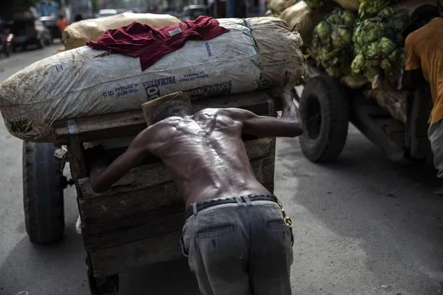 A porter pushes a loaded cart from the Croix de Bossales food market and makes his way through downtown Port-au-Prince, Haiti, Monday, October 4, 2021. (Photo by Rodrigo Abd/AP Photo)