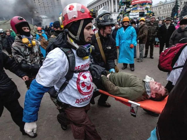 Anti government demonstrators carry a wounded comrade during clashes with riot police on the Independence square in Kiev, on February 20, 2014. (Photo by Yevgeny Maloletka/EPA)