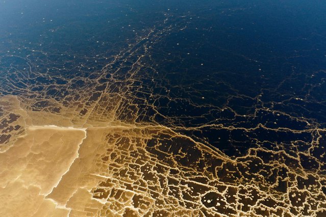 A picture taken on September 29, 2021, shows patterns formed by crystalized minerals on the surface of evaporation ponds of the Dead Sea, near the southern Israeli Moshav of Ein Tamar. A spectacular expanse of water in the desert, flanked by cliffs to east and west, the Dead Sea has lost a third of its surface area since 1960. The blue water recedes about a metre (yard) every year, leaving behind a lunar landscape whitened by salt and perforated with gaping holes. (Photo by Menahem Kahana/AFP Photo)