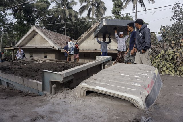 Villagers carry their belongings near a truck burried under volcanic ash from the Mount Semeru eruption at Sumber Wuluh village in Lumajang, East Java, Indonesia, 05 December 2021. (Photo by Ammar/EPA/EFE)