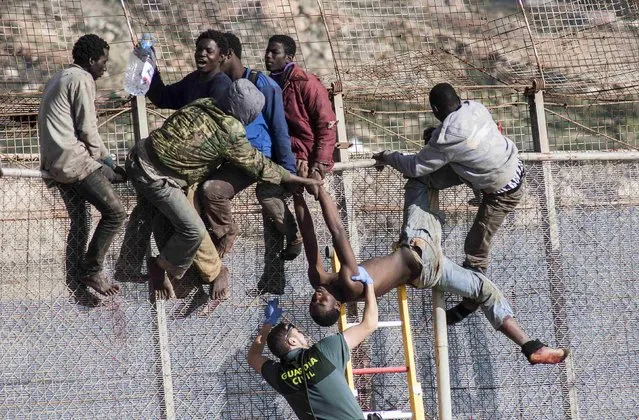 An African migrant is lowered down from a border fence by a Spanish Civil Guard as fellow migrants assist, at the border between Morocco and Spain's north African enclave of Melilla during the latest attempt to cross into Spanish territory, April 3, 2014. Spain has more than doubled the strength of security forces at Melilla, after about 500 people stormed its fences in the biggest border rush for years earlier this month. (Photo by Jesus Blasco de Avellaneda/Reuters)