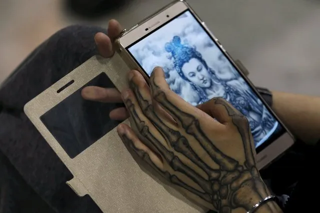 An exhibitor checks an image of Buddha on a mobile phone during an exhibition of 2016 Shanghai International Art Festival Of Tattoos in Shanghai, China, April 23, 2016. (Photo by Aly Song/Reuters)