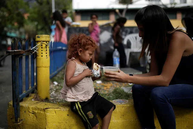 A volunteer of Make The Difference (Haz La Diferencia) charity initiative gives a cup of soup and an arepa to a homeless child  in a street of Caracas, Venezuela March 5, 2017. (Photo by Marco Bello/Reuters)