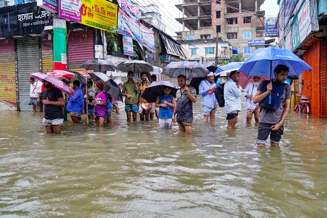 People carrying umbrellas, wade through a flooded street amid rainfall in Feni on August 22, 2024. (Photo by AFP Photo/Stringer)