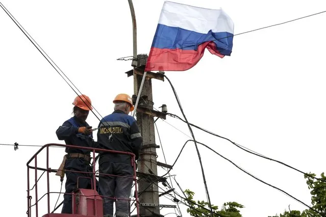 Municipal workers attach a Russian national flag to a pole preparing to celebrate 77 years of the victory in WWII in Mariupol, in territory under the government of the Donetsk People's Republic, eastern Ukraine, Thursday, May 5, 2022. Heavy fighting is raging at the besieged steel plant in Mariupol as Russian forces attempt to finish off the city's last-ditch defenders and complete the capture of the strategically vital port. (Photo by AP Photo/Stringer)