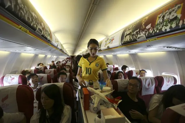 A flight attendant wearing a Brazil soccer team jersey serves passengers on an airplane travelling from Kunming to Hangzhou June 23, 2014. A Chinese airline company renovated the cabin of one of its flights then dressed the flight attendants with soccer jerseys as a way to celebrate the 2014 Brazil World Cup and hoping to attract more customers, local media reported. (Photo by Wong Campion/Reuters)