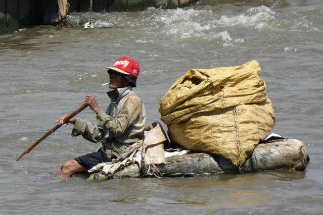 A scavenger sits on a raft as he attempts to collect recyclable materials in a river in downtown Jakarta, Indonesia on June 20, 2017. (Photo by Bay Ismoyo/AFP Photo)