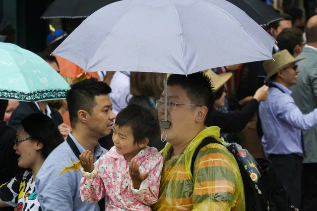 A man uses his mouth to hold an umbrella while carrying a child through a crowd and rain on the opening day of the Disney Resort in Shanghai, China, Thursday, June 16, 2016. (Photo by Ng Han Guan/AP Photo)