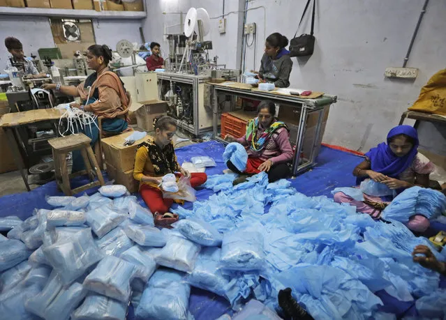 In this Saturday, February 1, 2020, photo, Indian laborers work at a surgical mask production unit in Ahmadabad, India. India has banned the export of all varieties of respiratory masks in view of a viral outbreak that began in China which has infected more than 14,550 people globally. (Photo by Ajit Solanki/AP Photo)