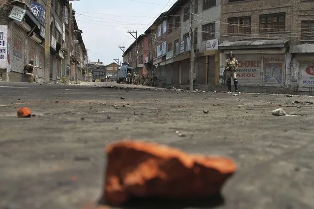 An Indian security officer stands guard as stones thrown at them litter a street in Srinagar, Indian controlled Kashmir, Sunday, July 10, 2016. Indian troops and protesters clashed in several parts of the state despite a curfew imposed in the Himalayan region following the killing of a popular rebel commander. (Photo by Mukhtar Khan/AP Photo)