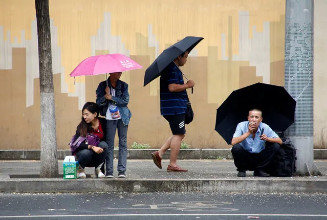 People hold umbrellas as they wait for a bus in Beijing, China July 15, 2016. (Photo by Thomas Peter/Reuters)