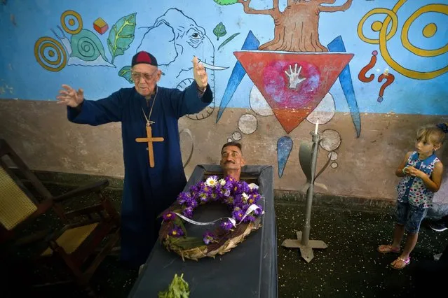 Marcelino Rogelio Estrada performs the role of a priest during the annual celebration known as the Burial of Pachencho, played by Divaldo Aguiar, who lies in a coffin during the mock funeral service, in Santiago de Las Vegas, Cuba, Sunday, February 5, 2017. Residents stage the mock funeral and burial of Pachencho in a boozy festival that has become an annual tradition to mark the end of the local carnival season. (Photo by Ramon Espinosa/AP Photo)