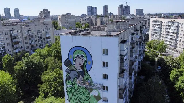A worker paints a “Saint Javelin”, a Virgin Mary holding an American-made anti-tank missile, in Kyiv, Ukraine, Tuesday, May 24, 2022. No matter where they live, the 3-month-old war never seems to be far away for Ukrainians. Those in towns and villages near the front lines hide in basements from constant shelling, struggling to survive with no electricity or gas — and often no running water. But even in regions out of the range of the heavy guns, frequent air raid sirens wail as a constant reminder that a Russian missile can strike at any time — even for those walking their dogs, riding their bicycles and taking their children to parks in cities like Kyiv, Kharkiv, Odesa and Lviv. (Photo by Natacha Pisarenko/AP Photo)
