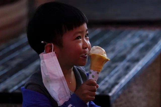 A child with a face mask eats ice cream outside an ice cream store on its first day of opening in Xianning, Hubei province, China on March 25, 2020. (Photo by Aly Song/Reuters)
