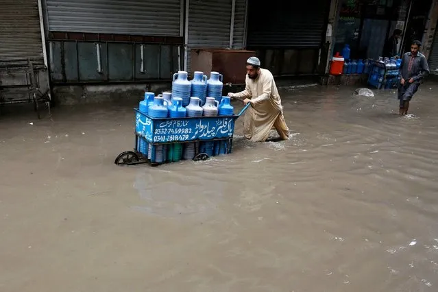A man pushes a cart of water cans wading across a flooded market place after heavy rainfall in Lahore on July 21, 2022. (Photo by Arif Ali/AFP Photo)