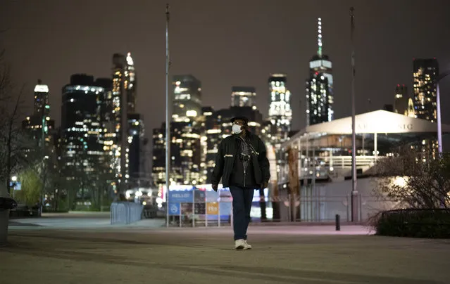 A man wearing a mask walks through Brooklyn Bridge Park, Tuesday night, April 14, 2020 during the coronavirus pandemic in New York. Known as “The City That Never Sleeps”, New York's streets are particularly empty during the pandemic. (Photo by Mark Lennihan/AP Photo)