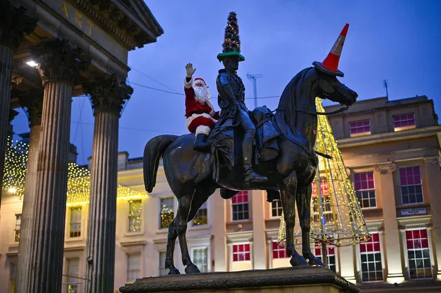 A man dressed in a Santa Claus suit scales the Duke of Wellington statue as Covid rules are tightened on December 21, 2021 in Glasgow, Scotland. First Minister Nicola Sturgeon announced a series of new pandemic-related rules today, to take effect from Dec. 26, with the aim of curbing the surge in Covid-19 infections. Among the restrictions are that large public events will be cancelled, new caps will be imposed on indoor and outdoor events, and hospitality venues can only offer table service. (Photo by Jeff J. Mitchell/Getty Images)
