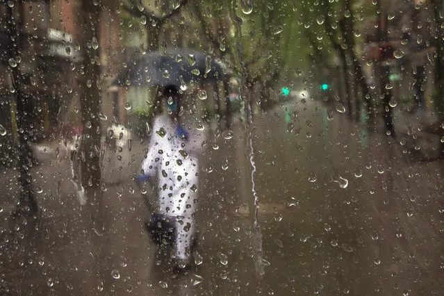 A primary care physician walks to visit a patient during a rainfall in Barcelona, Spain, Tuesday, April 21, 2020, as the lockdown to combat the spread of coronavirus continues. (Photo by Emilio Morenatti/AP Photo)