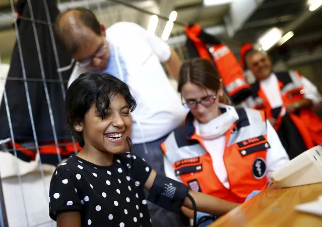 Shaima from Syria laughs as a doctor checks her blood pressure during her medical examination after her arrival in a former newspaper printing house used as a refugee registration centre for the German state of Hesse in Neu-Isenburg, on the outskirts of Frankfurt, Germany, September 11, 2015. (Photo by Kai Pfaffenbach/Reuters)