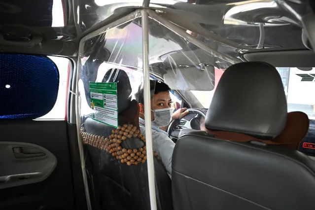 In this file photo taken on May 19, 2020 a taxi driver wearing a face mask looks on from behind a plastic screen as a preventive measure against the spread of COVID-19 novel coronavirus, in Hanoi. (Photo by Manan Vatsyayana/AFP Photo)