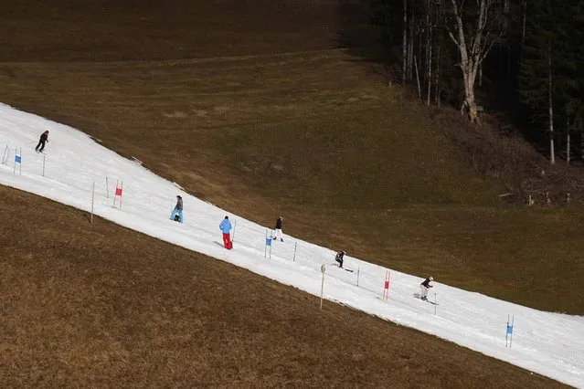 People skiing on a slope in Filzmoos south of Salzburg, Austria, Thursday, January 5, 2023. Sparse snowfall and unseasonably warm weather in much of Europe is allowing green grass to blanket many mountaintops across the region where snow might normally be. It has caused headaches for ski slope operators and aficionados of Alpine white this time of year. (Photo by Matthias Schrader/AP Photo)