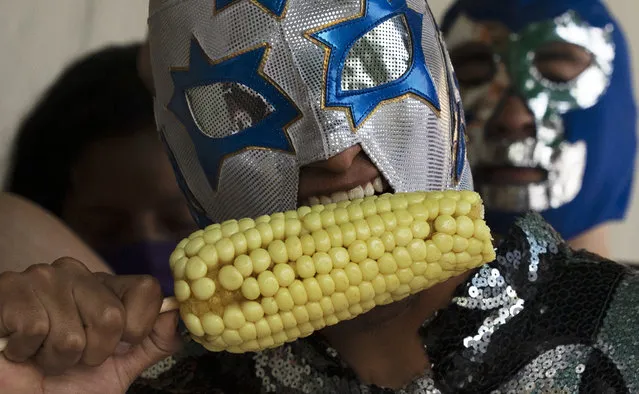 A Lucha Libre wrestler eats corn as he takes part in a health campaign promoting the use of masks amid the COVID-19 pandemic at the market in Xochimilco on the outskirts of Mexico City, Wednesday, August 19, 2020. Lucha Libre wrestlers whose deaths are publicly known to be from COVID-19 are Estrella Blanca Jr., Blackman II, Golden Bull, and Matematico II. (Photo by Marco Ugarte/AP Photo)
