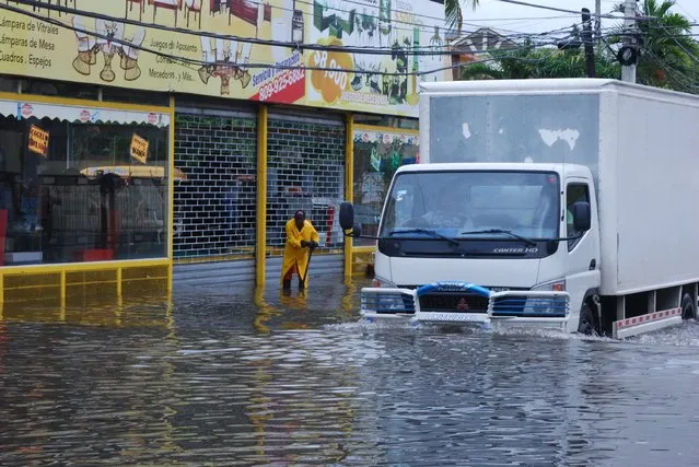 A sewage worker clears a sewer in a street flooded by the rains of Hurricane Matthew, in Santo Domingo, Dominican Republic, Tuesday, October 4, 2016. (Photo by Ezequiel Abiu Lopez/AP Photo)