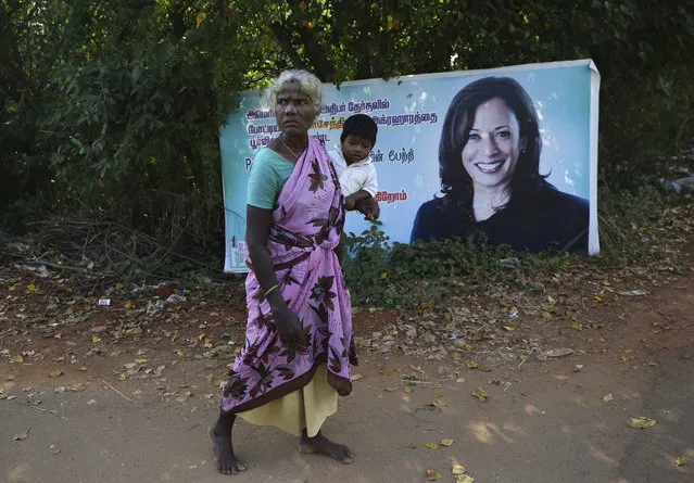 An Indian village woman carries a child and walks barefoot past a banner featuring U.S. democratic vice presidential candidate Sen. Kamala Harris in Thulasendrapuram village, south of Chennai, Tamil Nadu state, India, Tuesday, November 3, 2020. The lush green village is the hometown of Harris' maternal grandfather who migrated from there decades ago. (Photo by Aijaz Rahi/AP Photo)