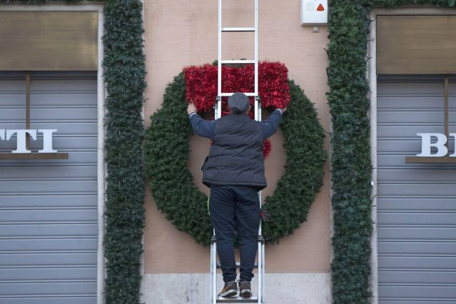 A person hangs a huge wreath on the facade of a building, as daily life continues amid the second wave of the Covid-19 coronavirus pandemic in downtown Rome, Italy, 22 November 2020. Italy fights with the second wave of pandemic of the SARS-CoV-2 coronavirus which causes the Covid-19 disease. (Photo by Massimo Percossi/EPA/EFE)