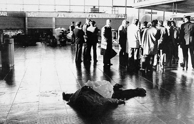 The body of a victim of the terrorist attack at Rome's Leonardo Da Vinci airport, December 27, 1985 lies on the floor of the international terminal as investigators stand nearby. In the left background is the bar where a grenade exploded. (Photo by Gianni Foggia/AP Photo)