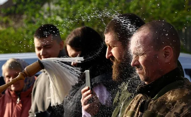 Faithful are sprinkled with holy water by Ukrainian military chaplain Dionisii, as he holds a service for servicemen and civilians to celebrate Orthodox Easter on the streets of Druzhkivka, Ukraine on April 16, 2023. (Photo by Kai Pfaffenbach/Reuters)