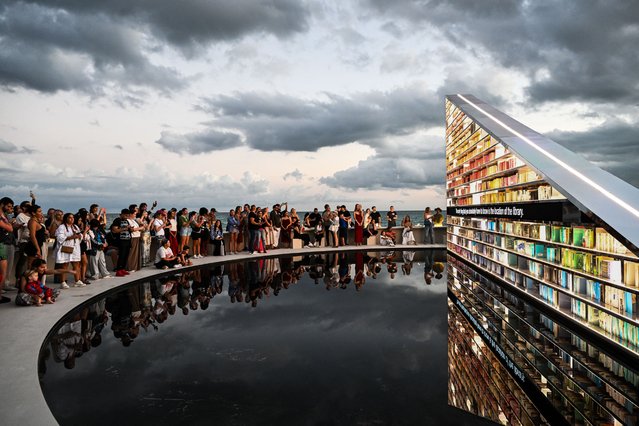 People look at the exhibition “LIBRARY OF US” by British artist Es Devlin, a 50-foot-wide rotating triangular bookshelf containing 2,500 books that have shaped the artist's life and practice, during Art Basel 2025, in Miami Beach, Florida, December 2, 2025. (Photo by Chandan Khanna/AFP Photo)