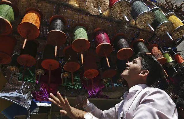 An Indian vendor winds strings for kites as he waits for customers at his shop ahead of the Hindu festival of Makar Sakranti, also knowns as kite festival, in Hyderabad, India, Monday, January 12, 2015. Kites are flown in many parts of India during the Hindu festival of Makar Sakranti to be celebrated on Jan. 14 to mark the transition of winter to spring. (Photo by Mahesh Kumar A./AP Photo)